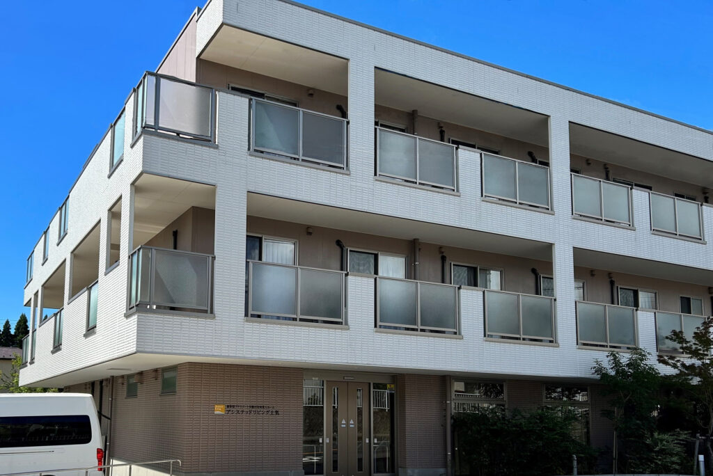 白タイル張りの3階建て介護施設。複数のバルコニーと大きな窓が特徴。