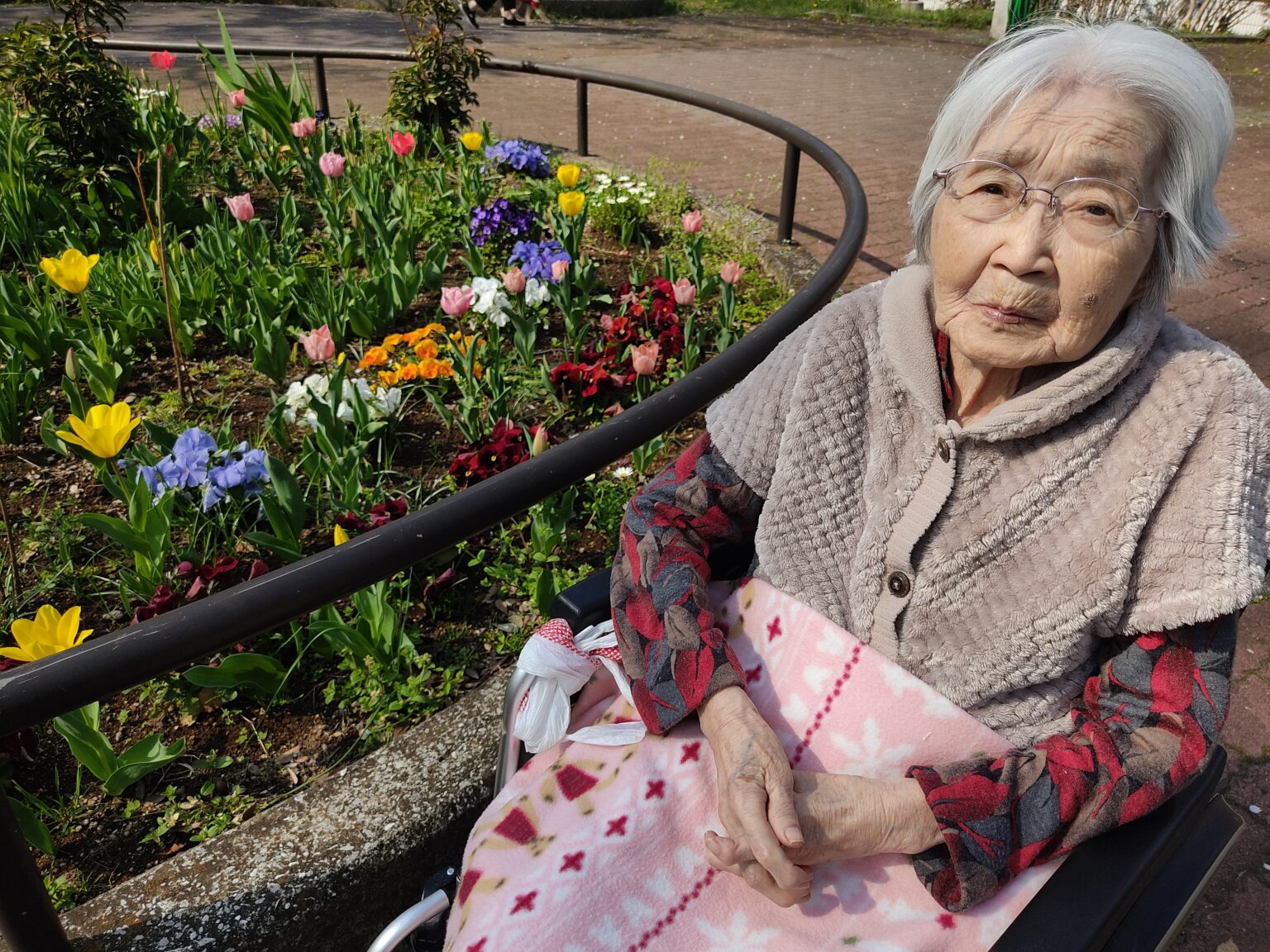 入居者が花壇の前でくつろぐ様子。季節の花々に囲まれた施設の庭園。